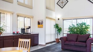A spacious room with a dark wooden dining table, a purple sofa, and a large window with blinds. - Motel 6 Madras, OR (Madras)