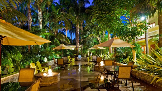An outdoor patio area with tables and chairs, surrounded by lush greenery and palm trees. - Ocean Palms Beach Resort (Carlsbad)