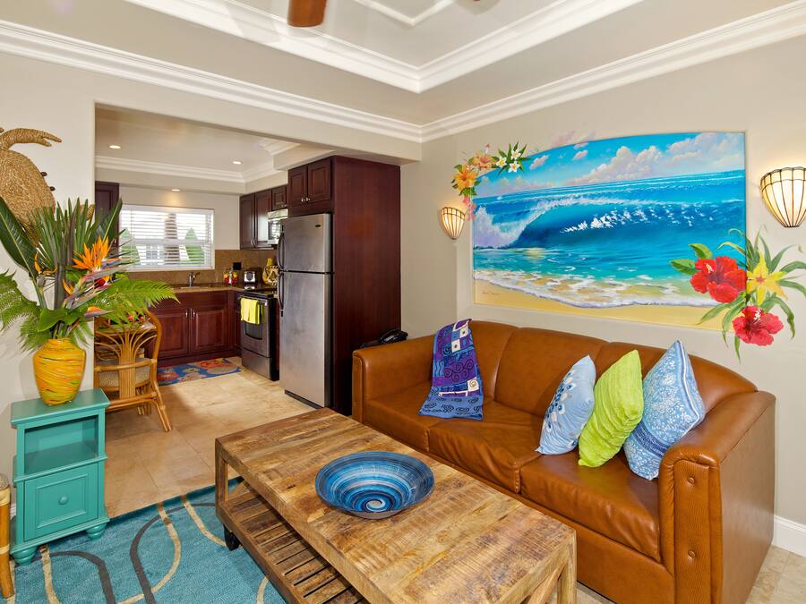 A living room with a brown leather sofa, a wooden coffee table, and a painting of a beach scene.