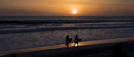 A beach scene with two people carrying surfboards, a sunset, and waves.