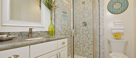 A modern bathroom with a glass-enclosed shower, a sink with a vase of flowers, and a toilet with a towel stack.