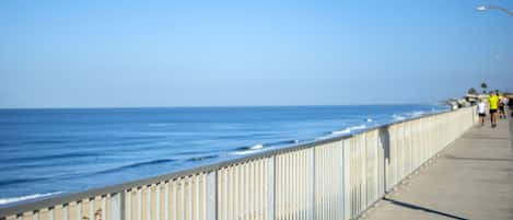 A coastal walkway with a metal railing, a clear sky, and the ocean in the background.