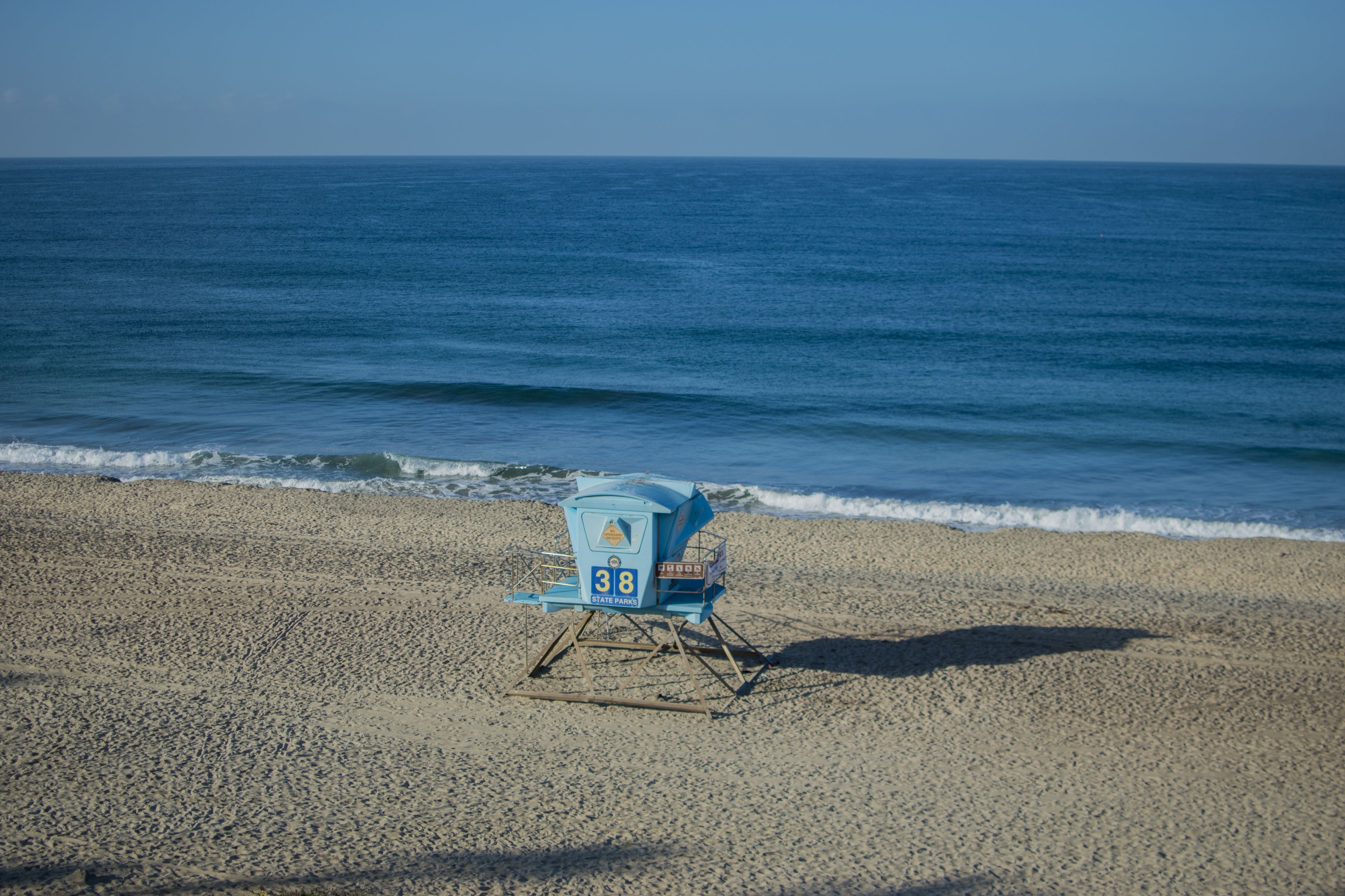 Ein Liegestuhl am sandigen Strand, im Hintergrund das Meer.
