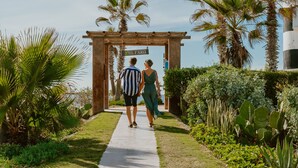 A couple walking through a garden pathway leading to a wooden archway with a sign that reads "EL FARO".