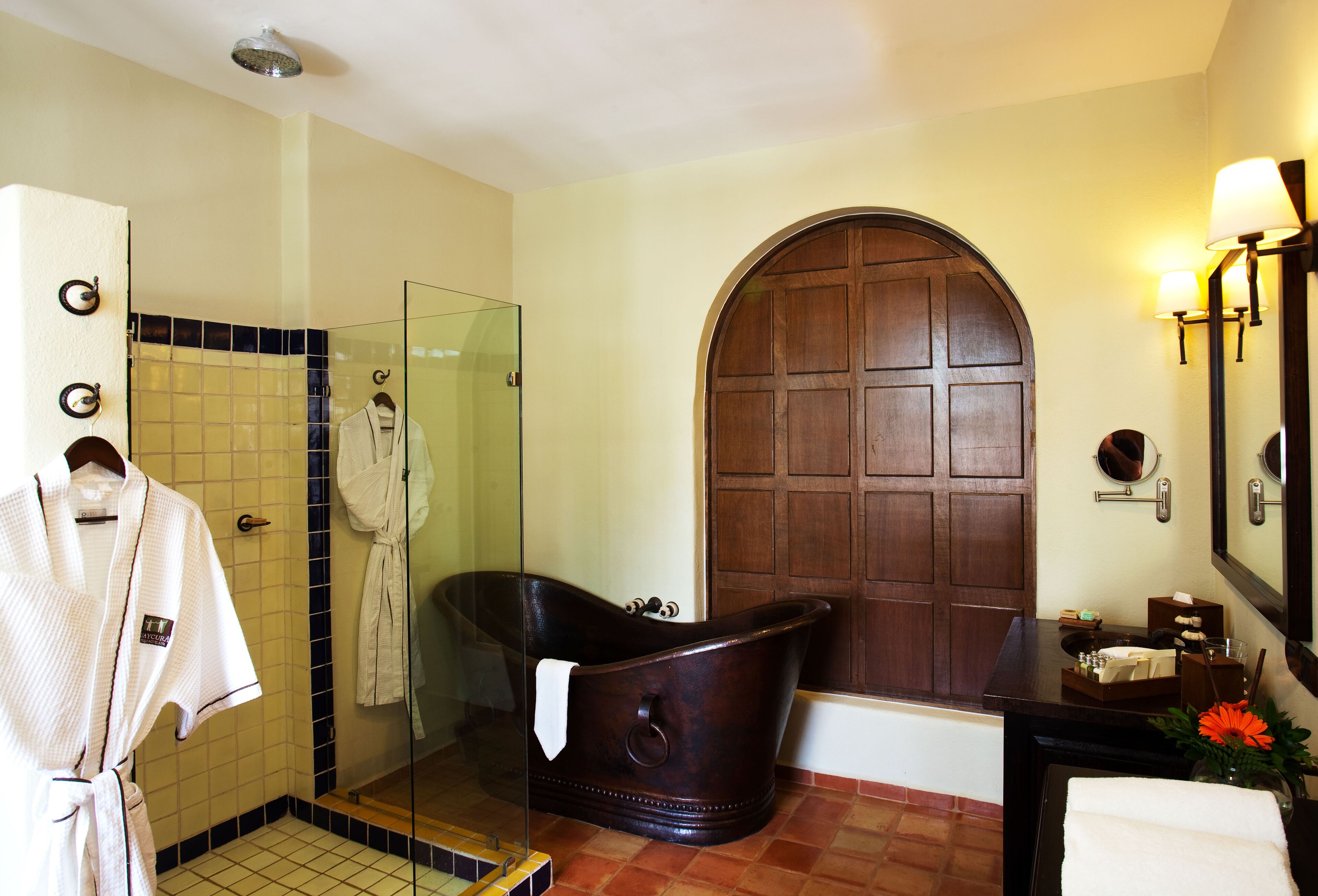 A bathroom with a glass shower enclosure, a wooden door, a bathtub, and a vanity with a mirror.