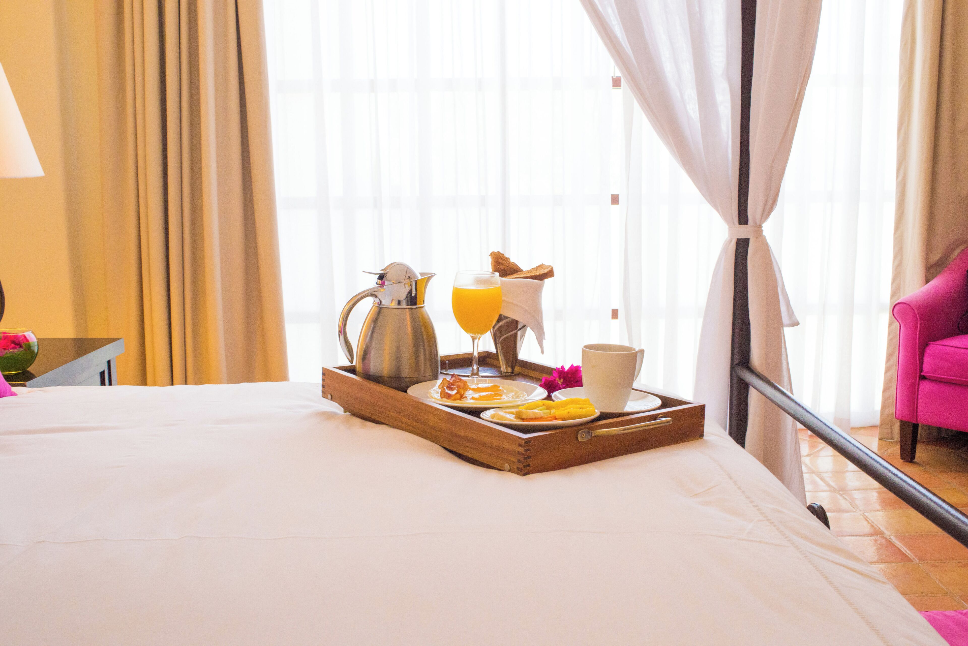 A neatly made bed with a tray of breakfast items including toast, orange juice, and a coffee pot.