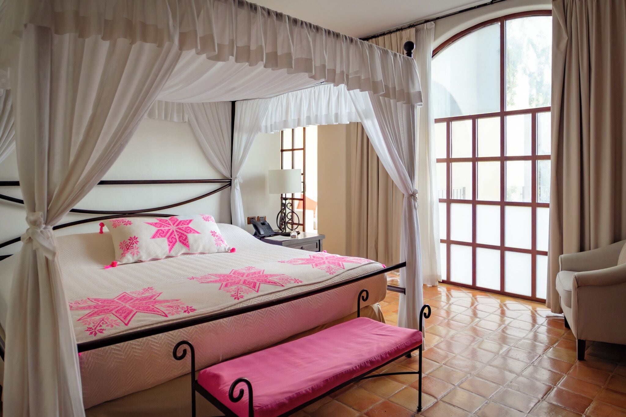 A bed with a canopy, a bedside table with a lamp, and a chair.