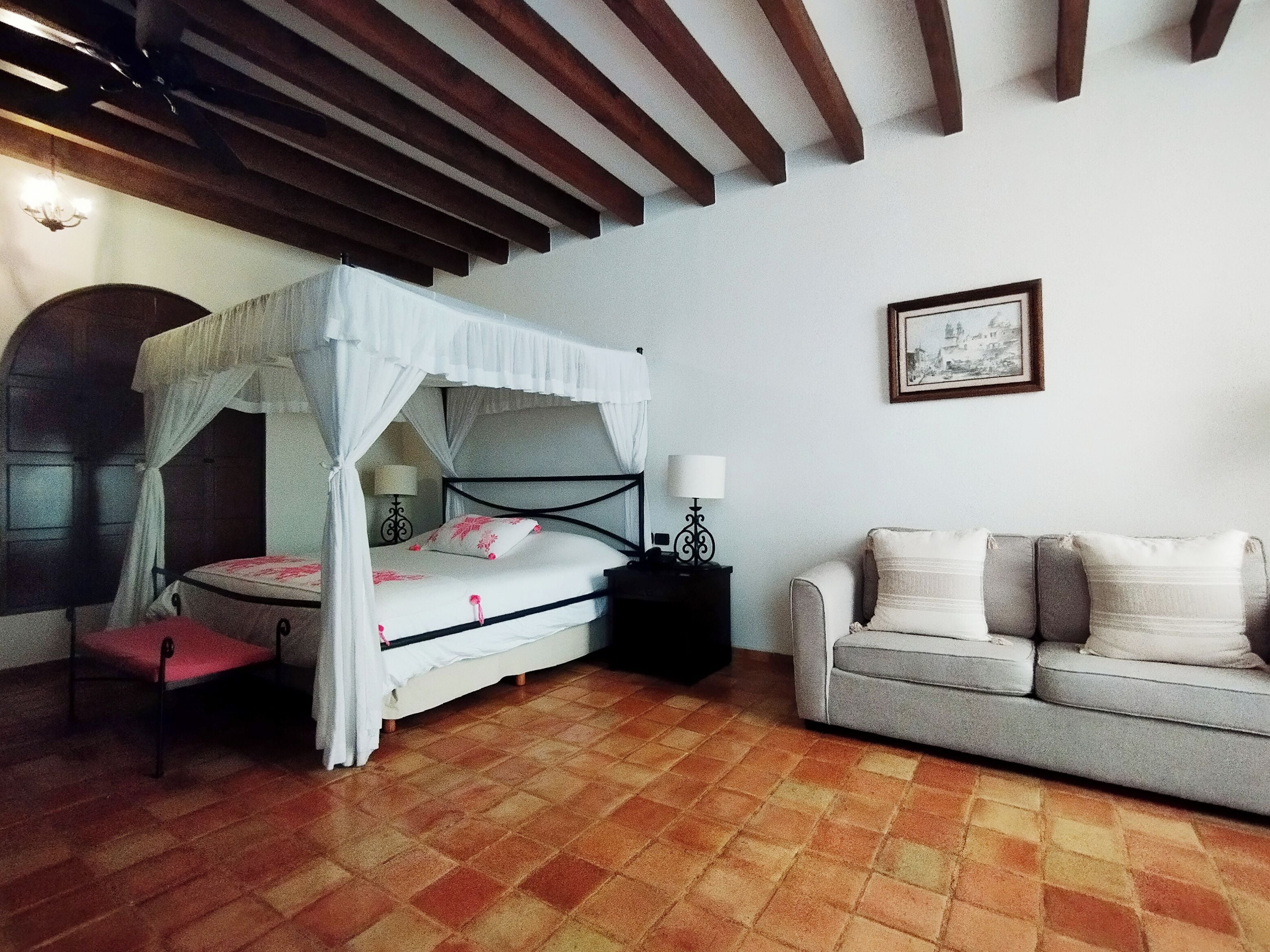 A bedroom with a four-poster bed, a sofa, a nightstand, and a framed picture on the wall.