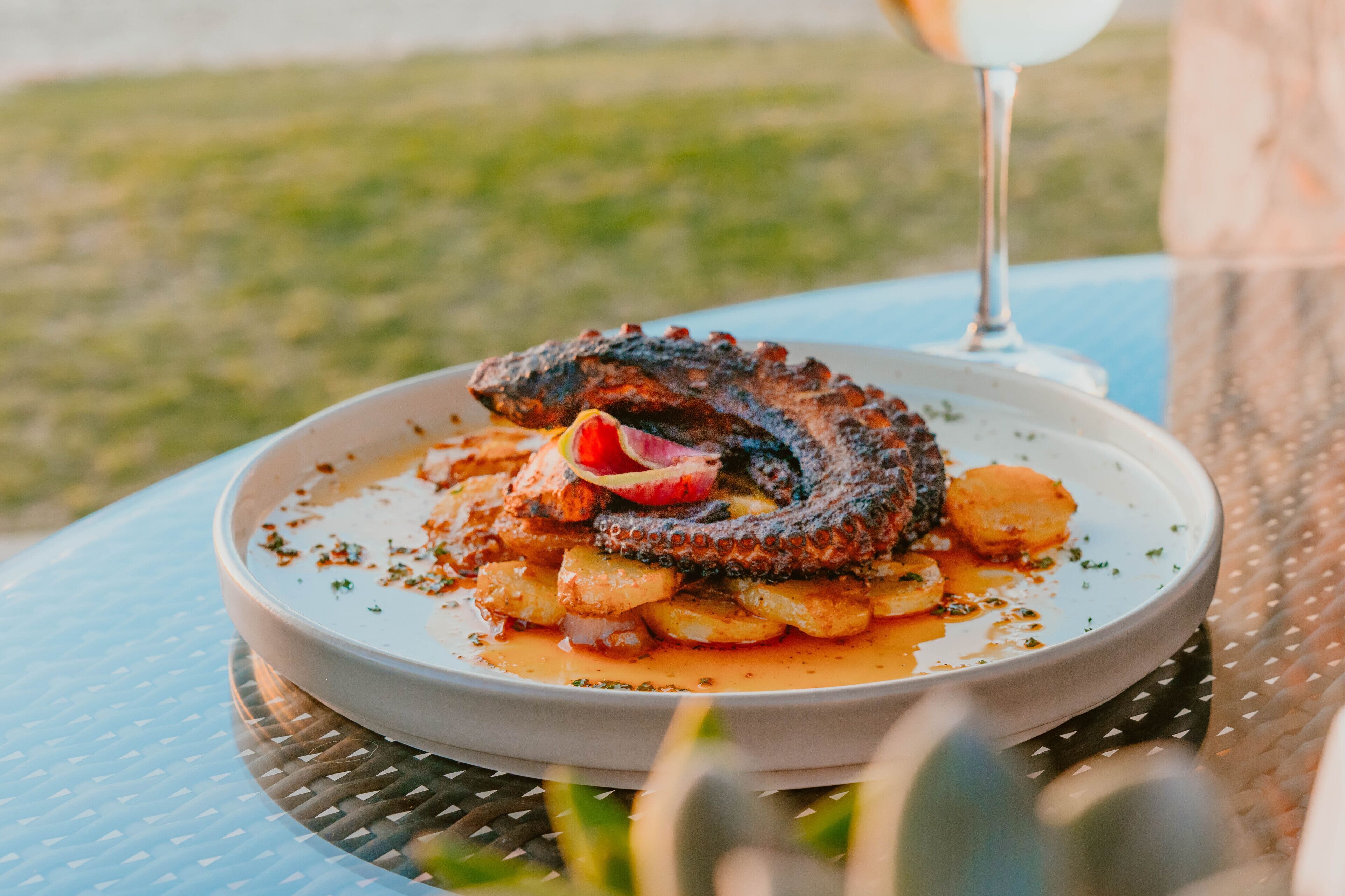 Un plat de fruits de mer servi dans une assiette, accompagné d’un verre de vin blanc, sur une table à l’extérieur.