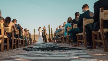 A wedding ceremony on a beach with wooden chairs arranged in rows.