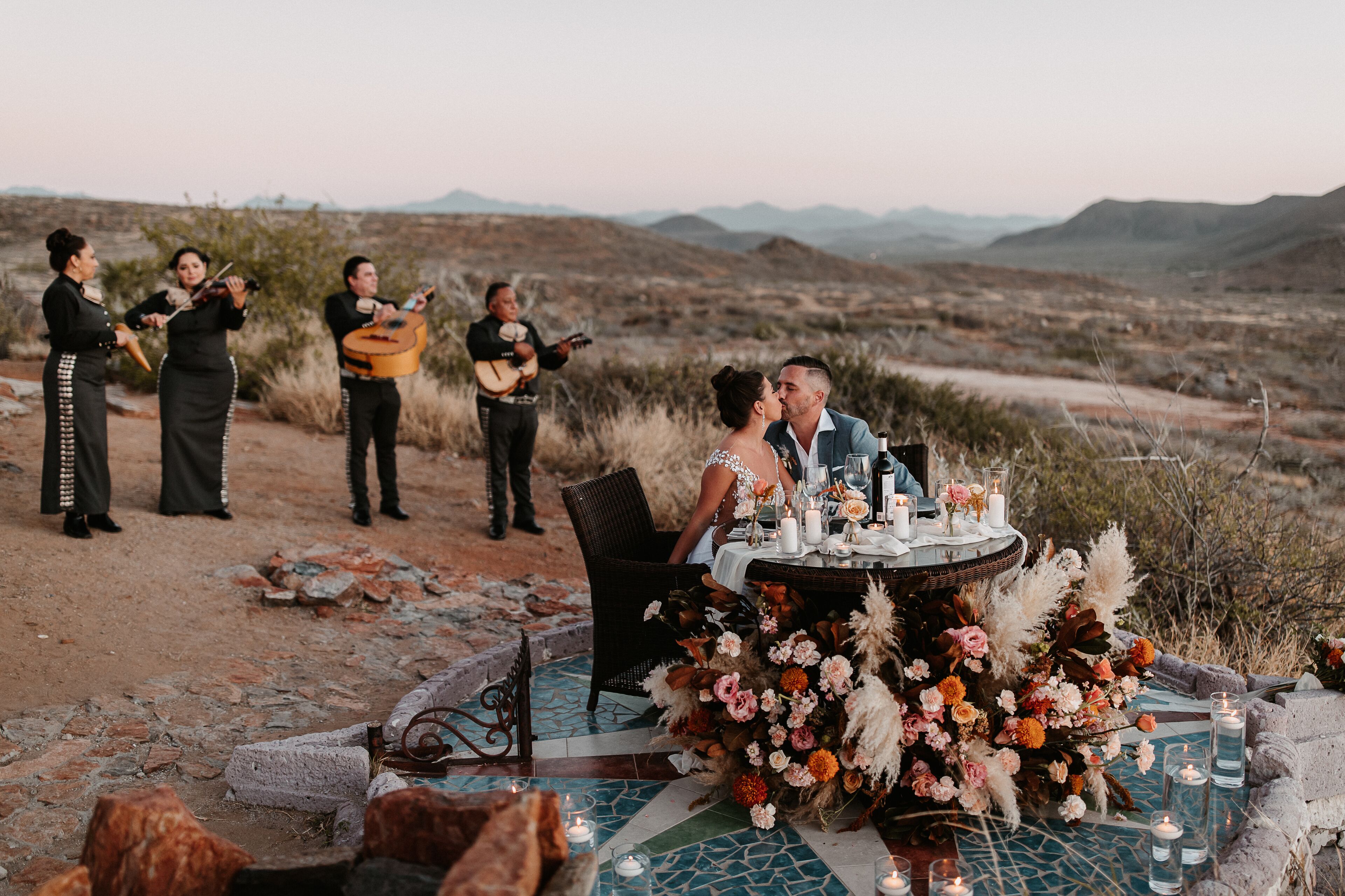 A wedding ceremony outdoors with a decorated table and musicians in the background.