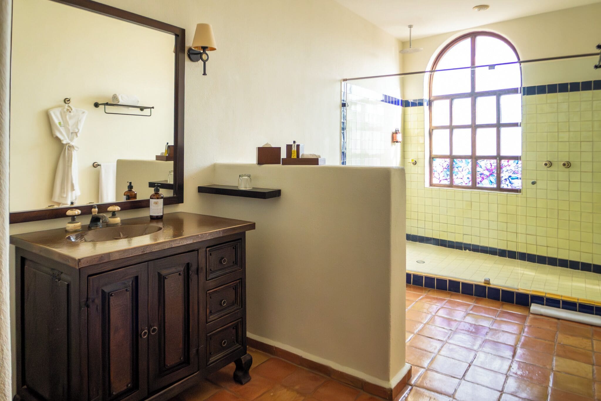 A bathroom with a dark wooden vanity, a large mirror, a window with a view, and a tiled shower area.