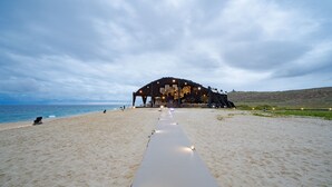 A beach with a white pathway leading to a large, dark structure with multiple levels and lights.