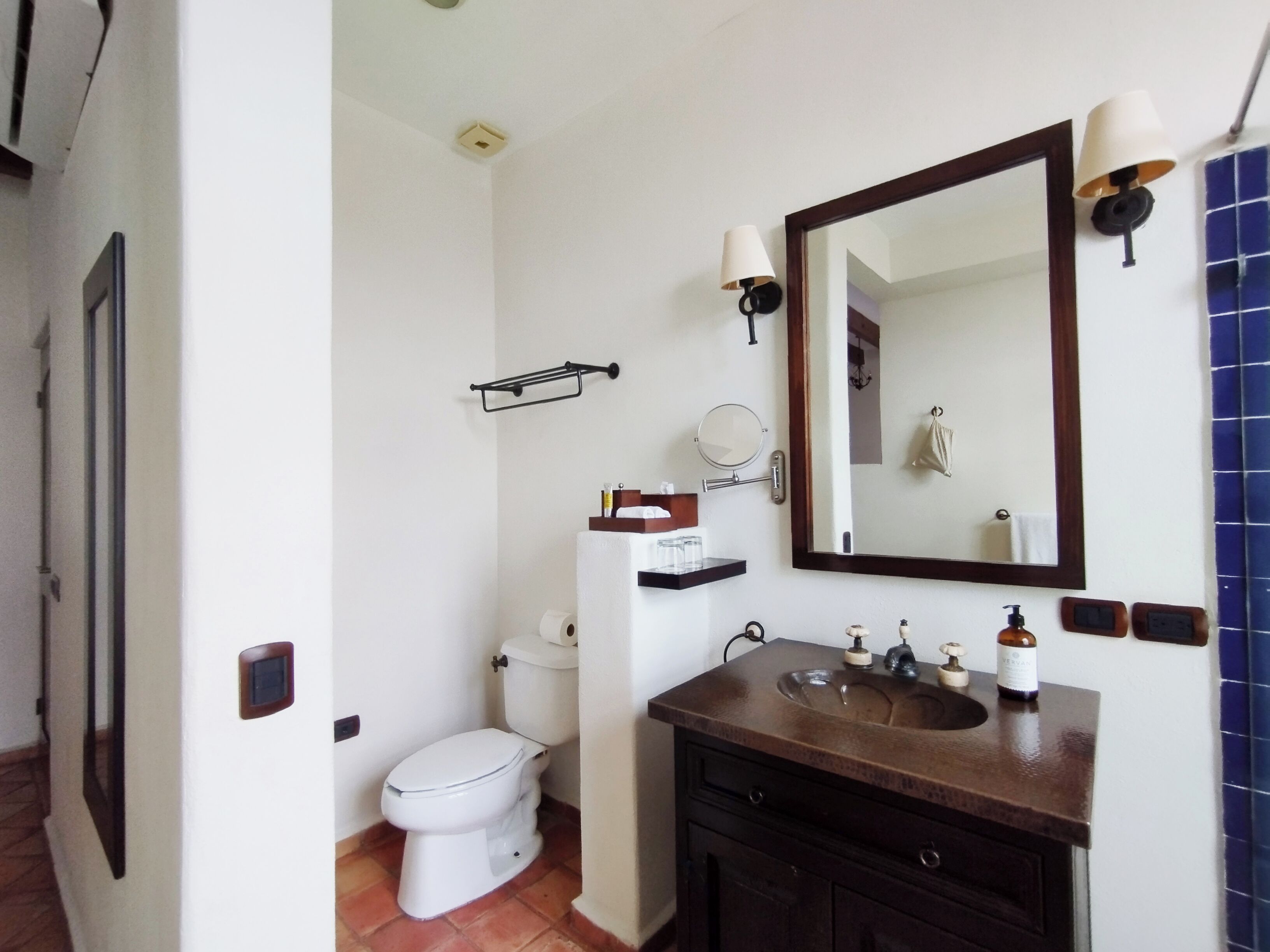 A bathroom with a white toilet, a sink with a dark countertop, a large mirror, and a towel rack.