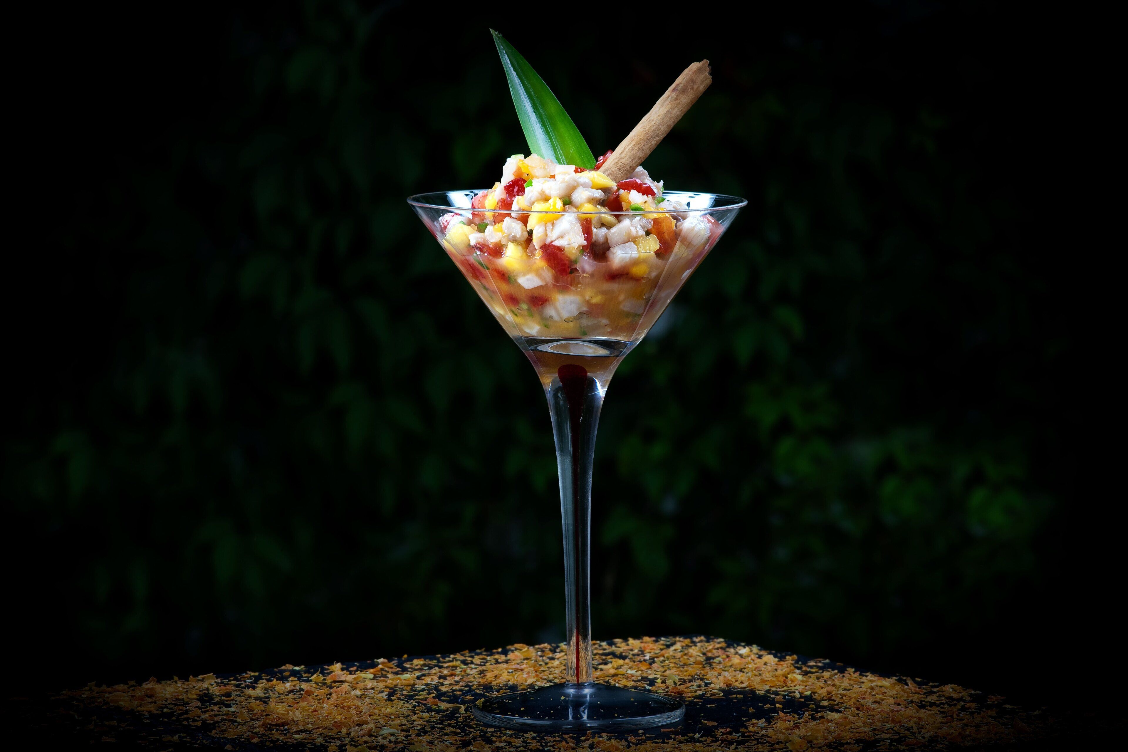 A cocktail in a martini glass with a garnish, set against a dark background.