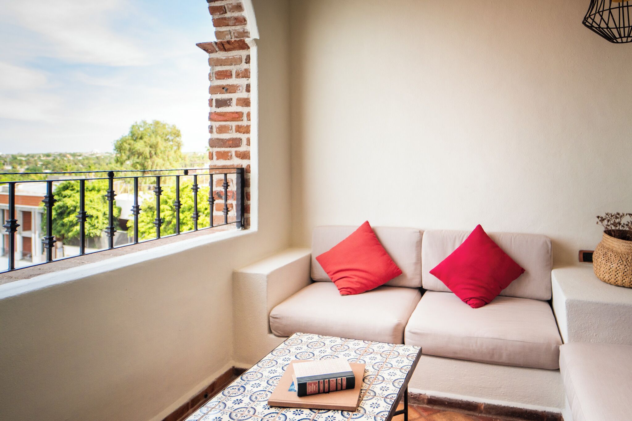A balcony with a beige sofa, two red cushions, and a patterned table with books.