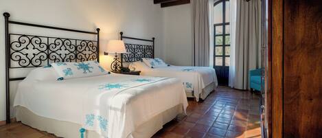 A room with two beds, a wooden ceiling, a window with curtains, and a nightstand with a lamp.