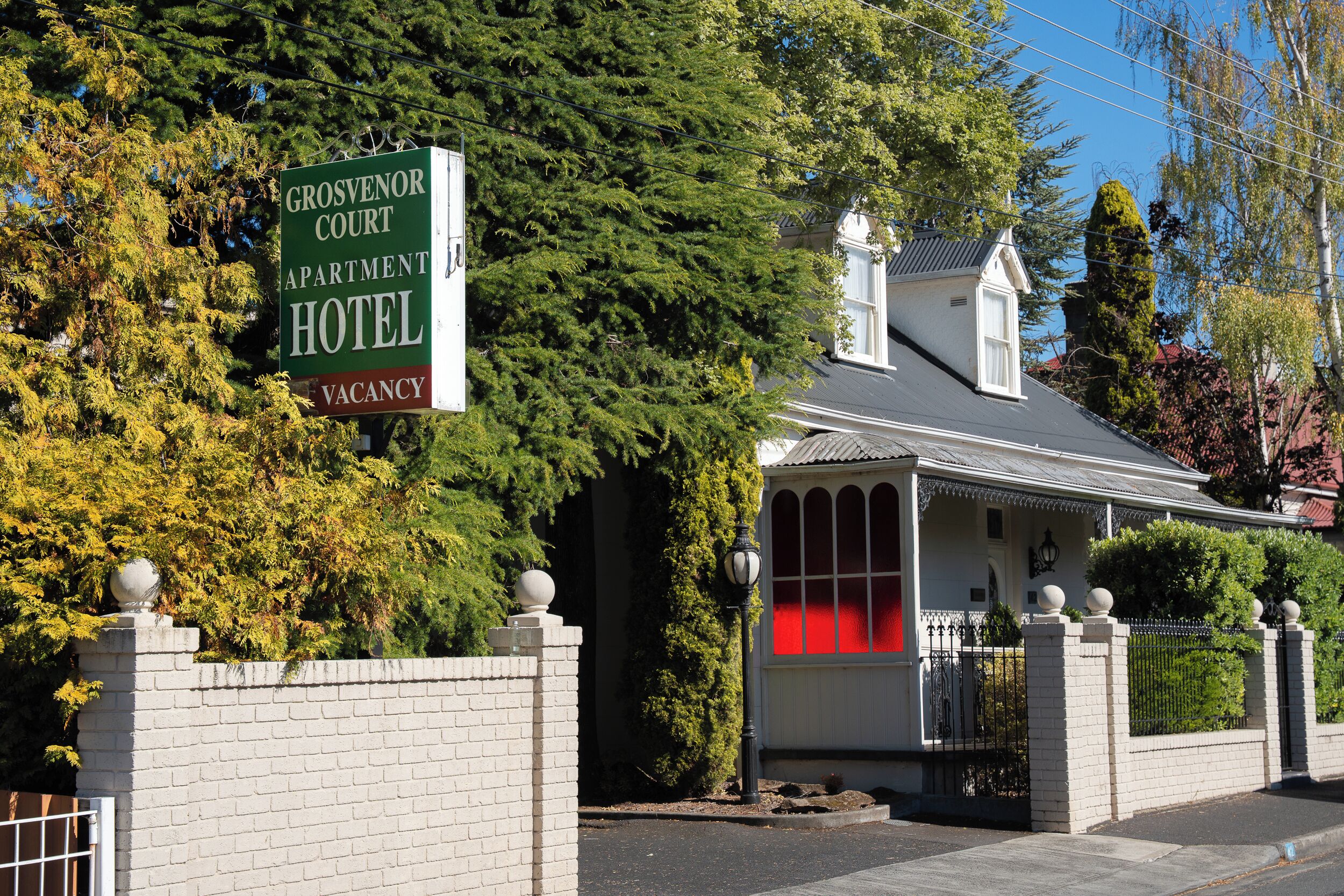 A sign for Grosvenor Court Apartment Hotel with a brick wall and a gated entrance.