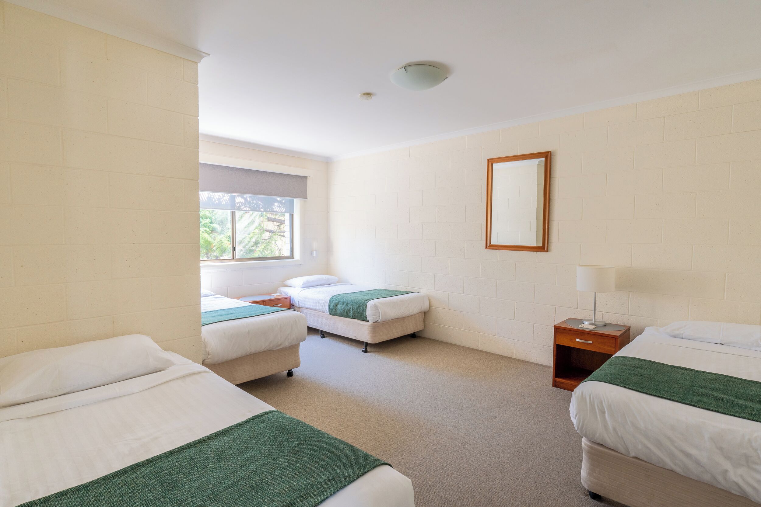 A hotel room with two single beds, a small wooden nightstand, a window, and a mirror on the wall.