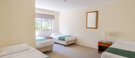 Una habitación de hotel con dos camas individuales, una mesita de noche de madera, una ventana y un espejo en la pared.