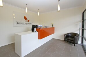 A reception desk with a white and orange color scheme, a black leather chair, and a framed sign above the desk. - Grosvenor Court Apartments Hobart (Sandy Bay)