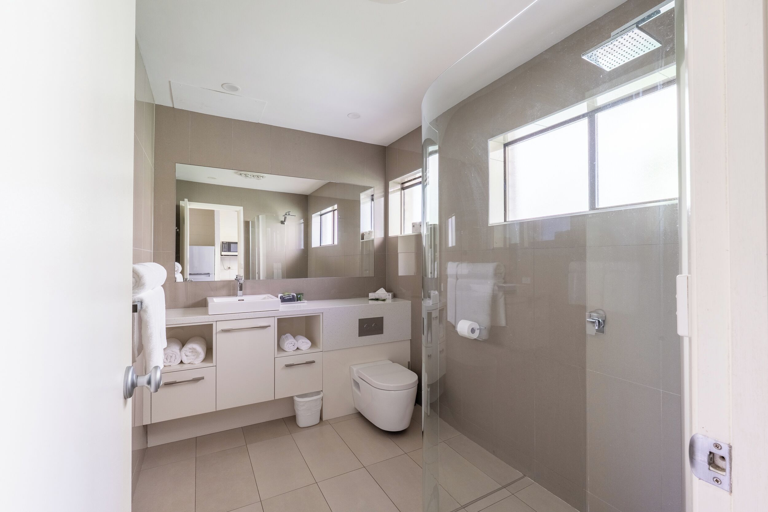 Een moderne badkamer met een glazen douchecabine, toilet, wastafel met spiegel en een handdoekrek.