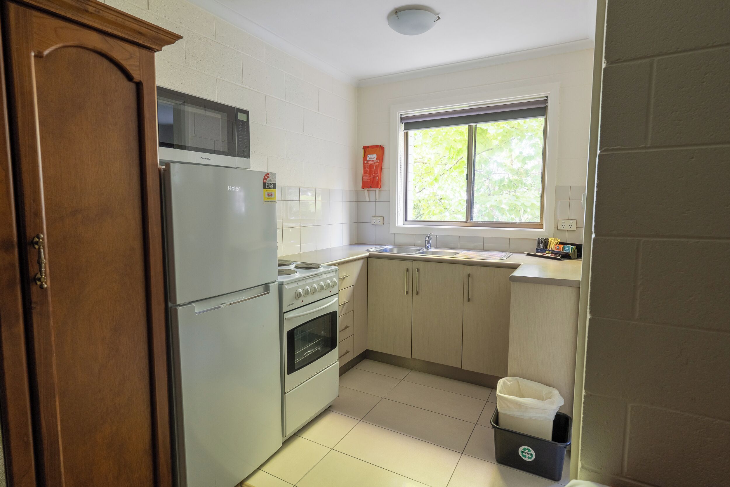 A compact kitchen with a refrigerator, stove, microwave, and a window with blinds.
