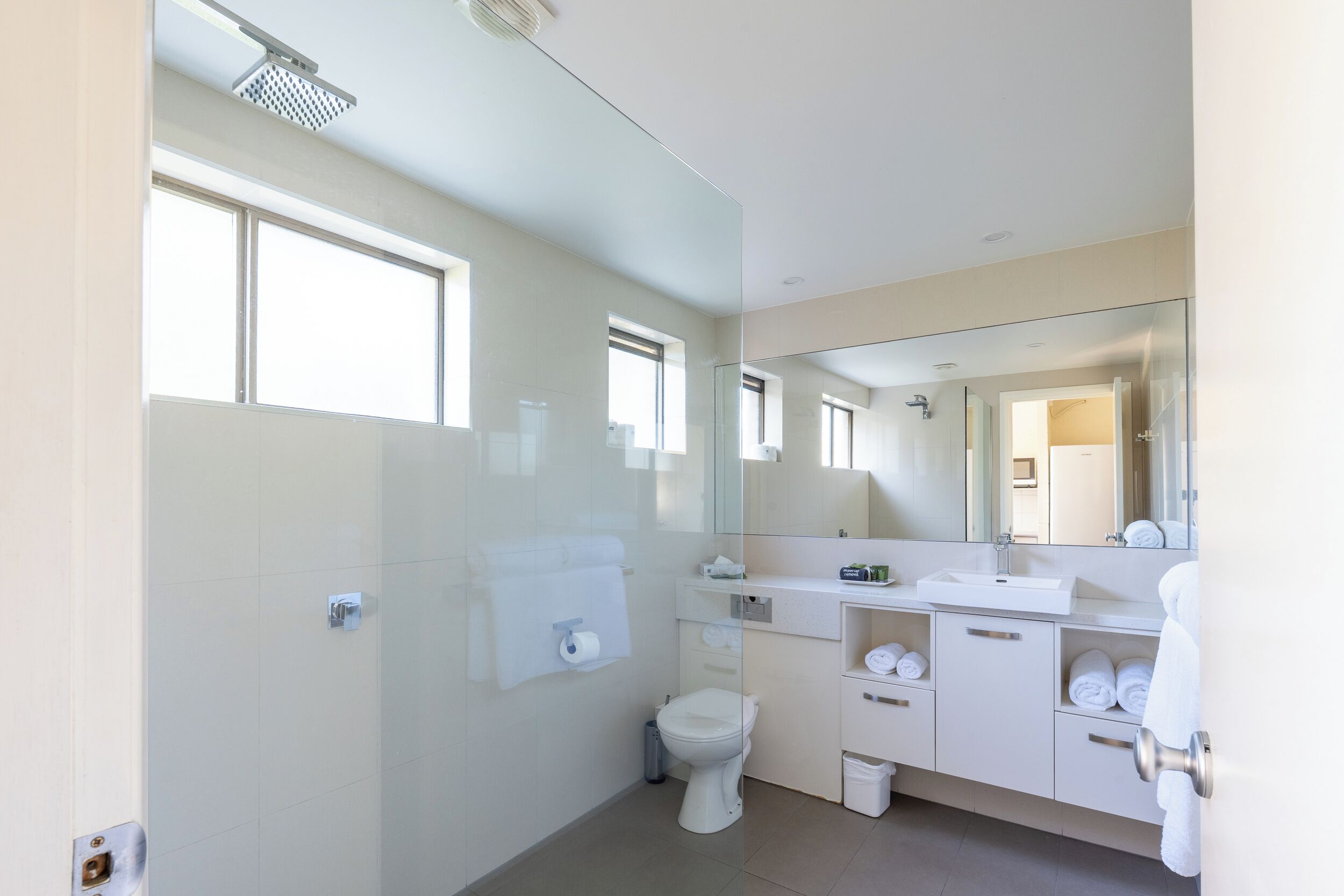 A modern bathroom with a glass shower enclosure, a toilet, a sink with a mirror, and a towel rack.