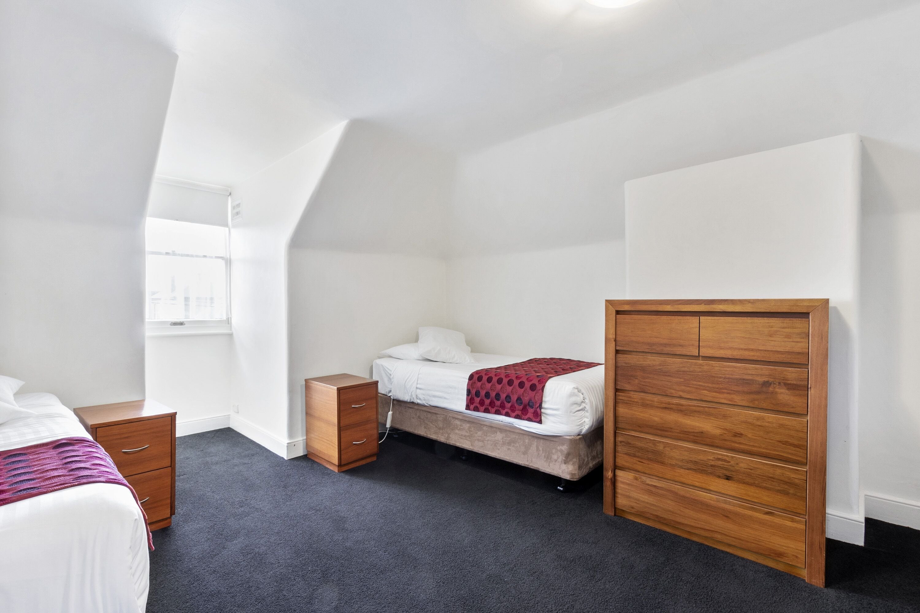 A bedroom with a bed, a wooden dresser, a small cabinet, and a window.