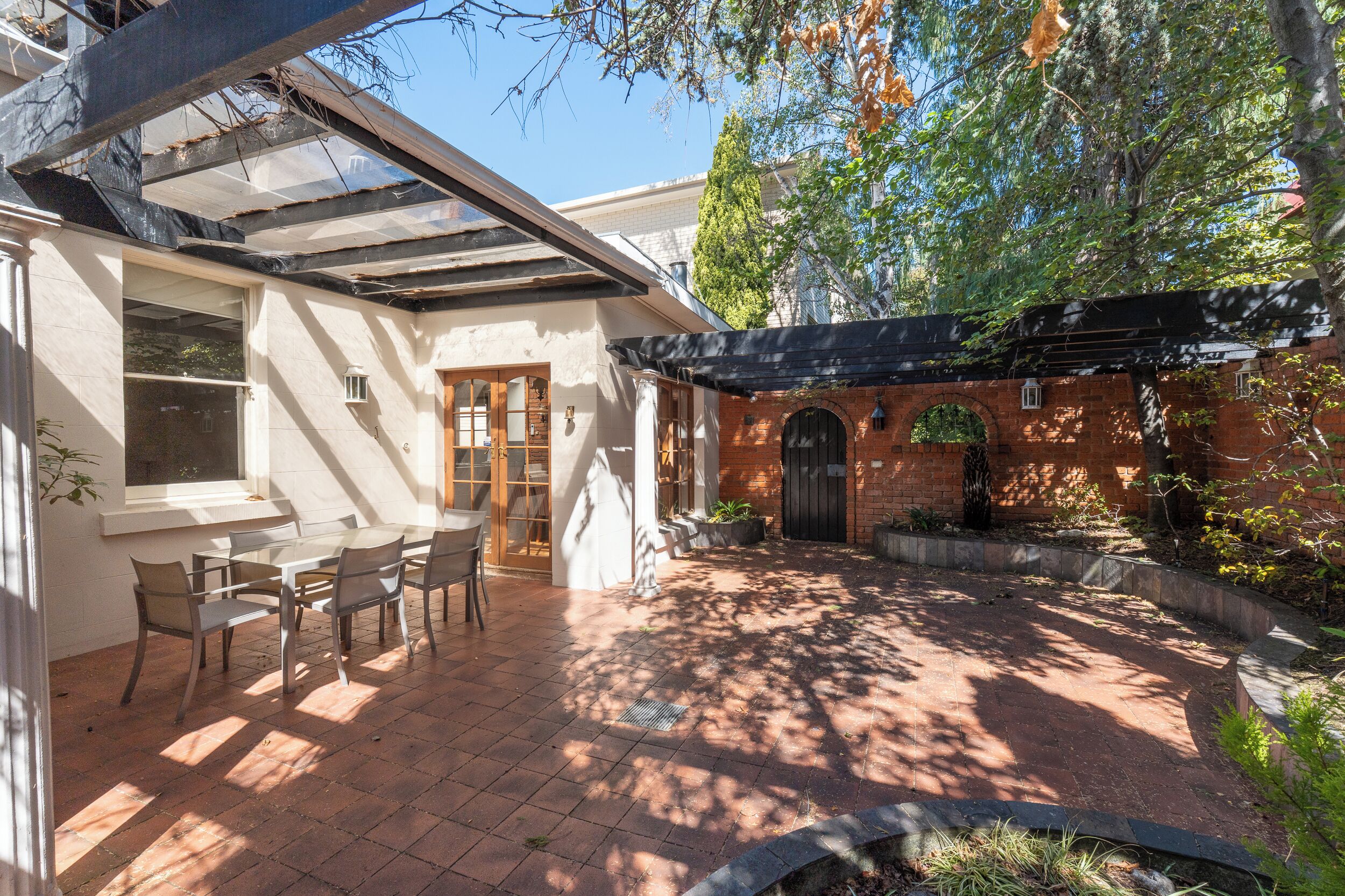 A covered patio area with a table and chairs, a brick wall, and a pergola.