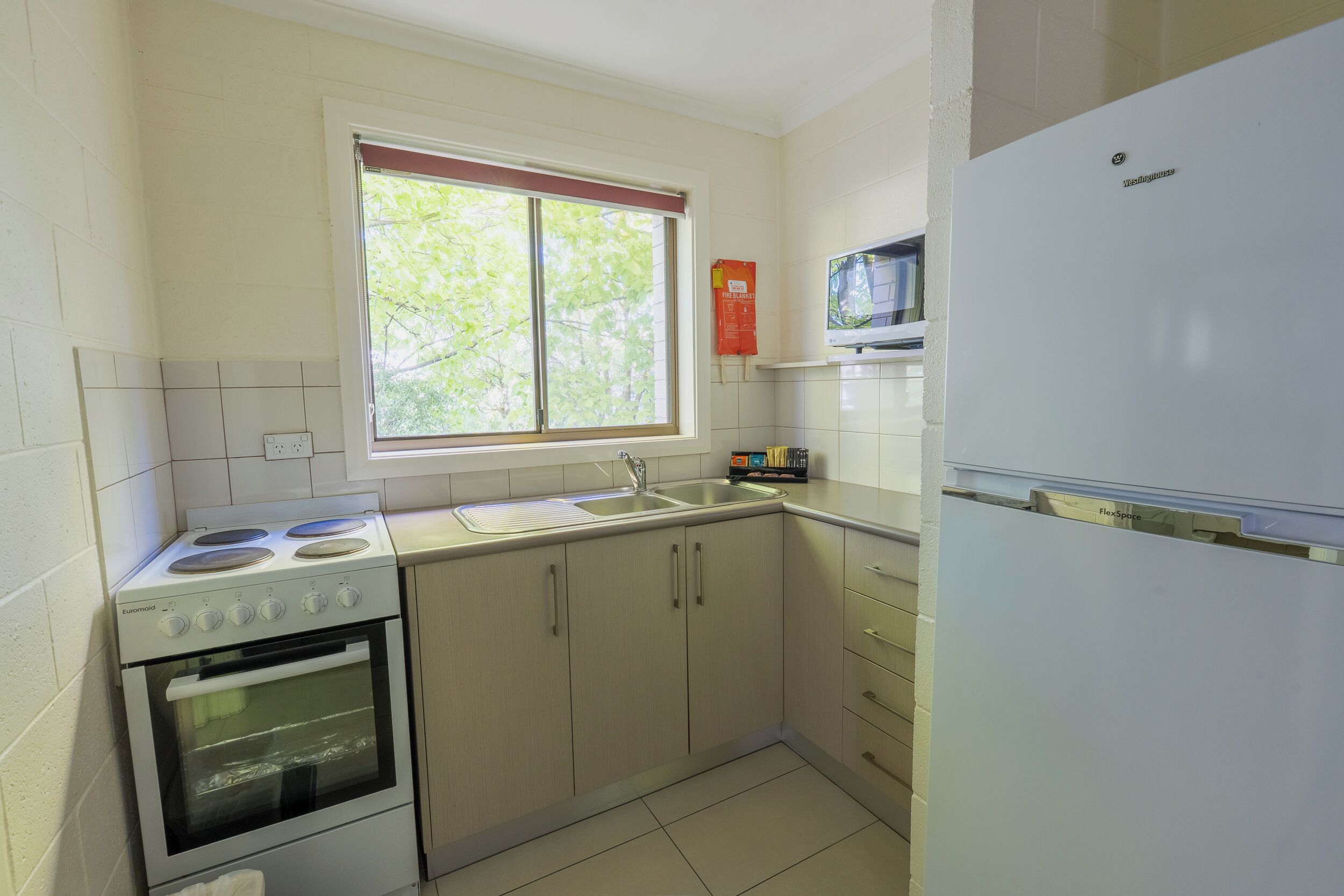 A kitchen with a stove, oven, sink, and a window with a view of trees.
