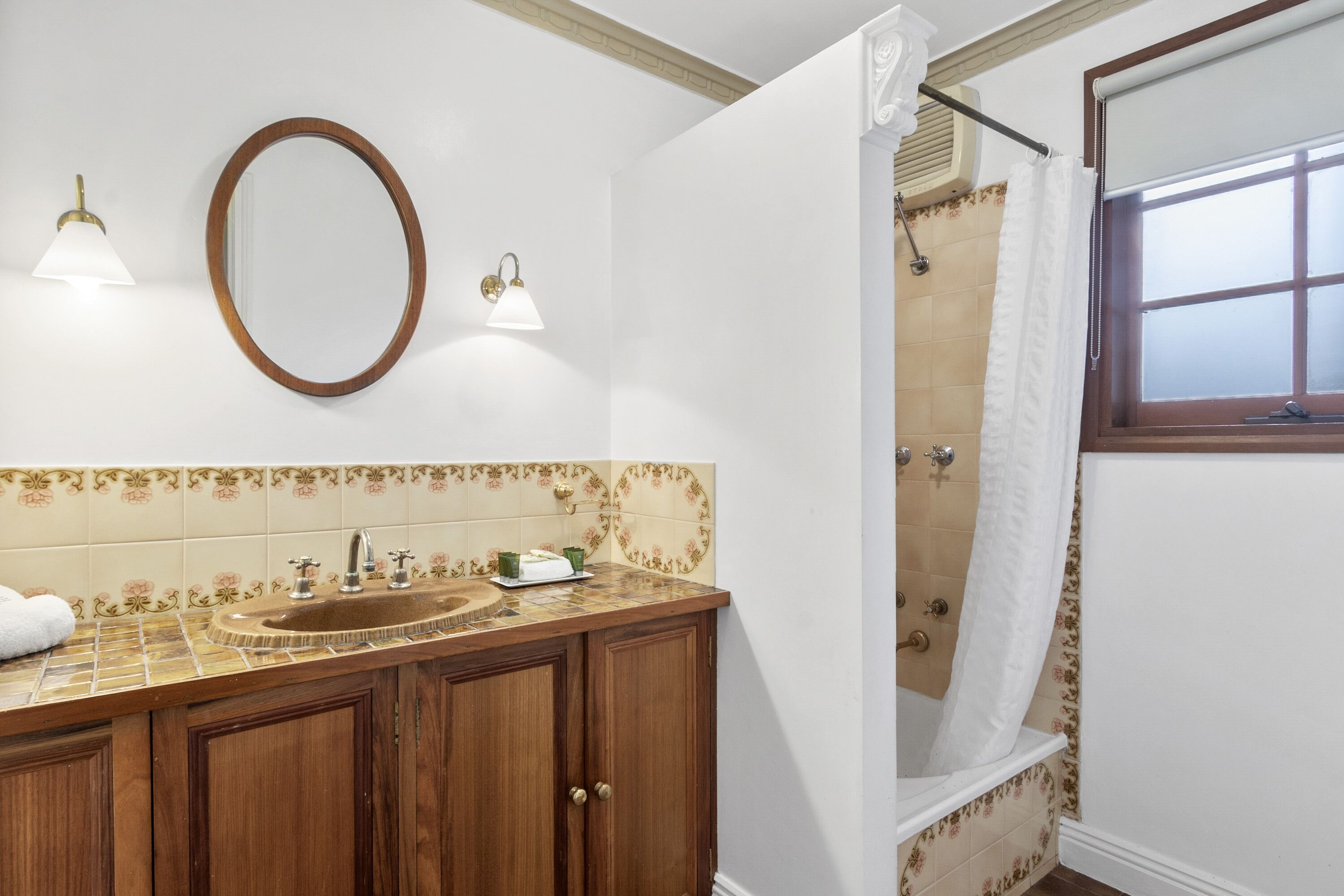 A bathroom with a wooden vanity, a sink, a mirror, a shower with a curtain, and a window.