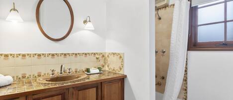 A bathroom with a wooden vanity, a sink, a mirror, a shower with a curtain, and a window.