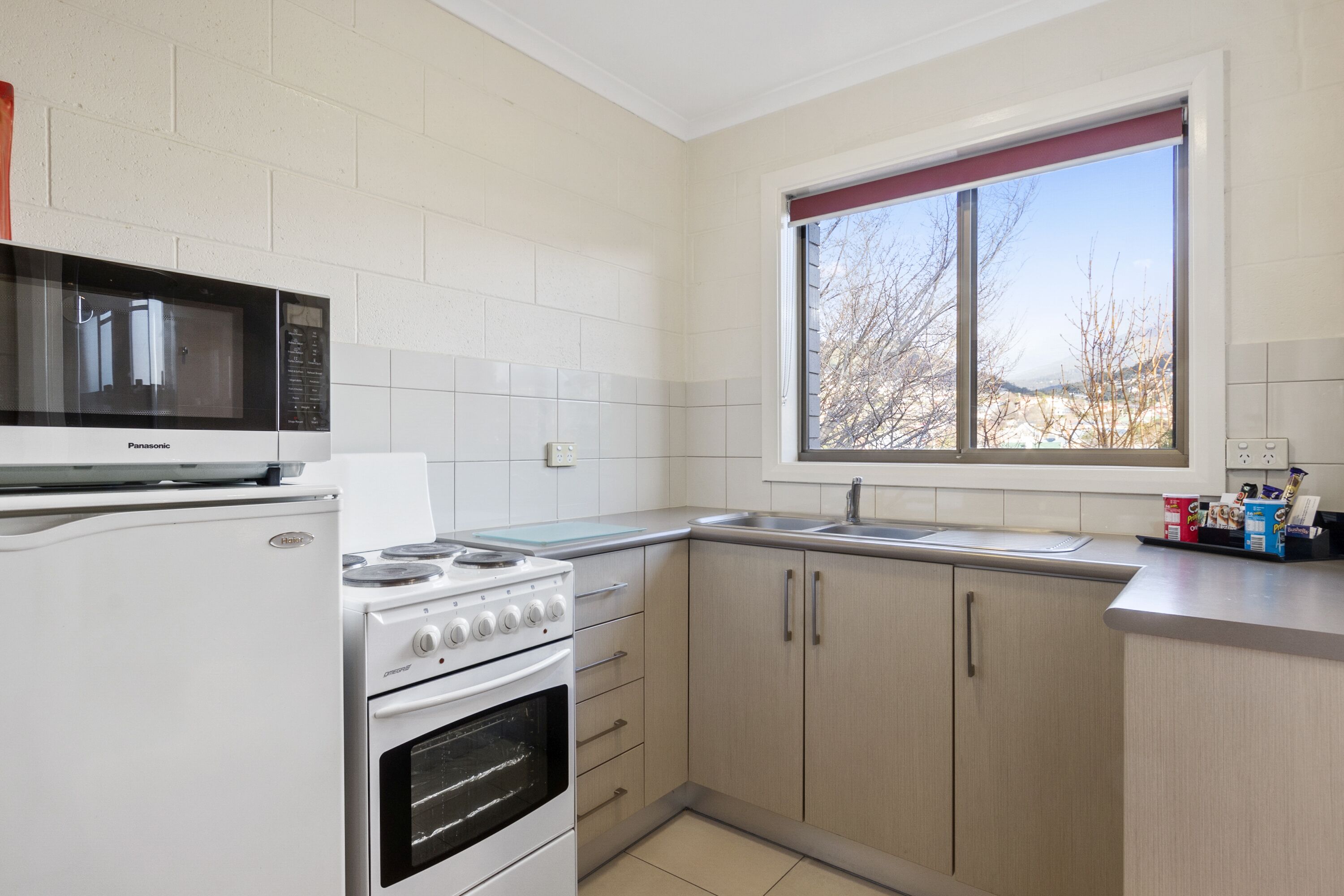 A compact kitchen with white appliances, a window with a view, and light-colored cabinets.