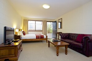 A hotel room with a bed, a television, a leather sofa, and a wooden table. - Grosvenor Court Apartments Hobart (Sandy Bay)