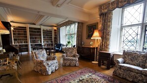 A library with bookshelves, a reading area with chairs, a patterned rug, and large windows with curtains. - Tower (Mold)