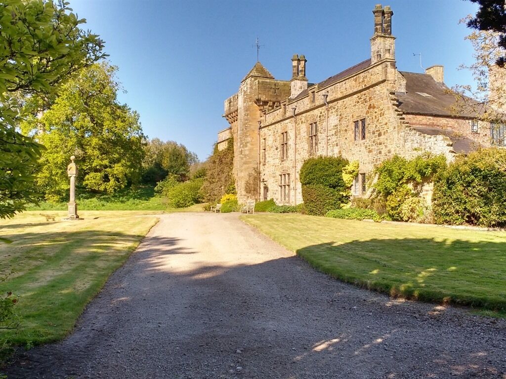 A historic stone building with a gravel driveway leading to a well-maintained lawn.