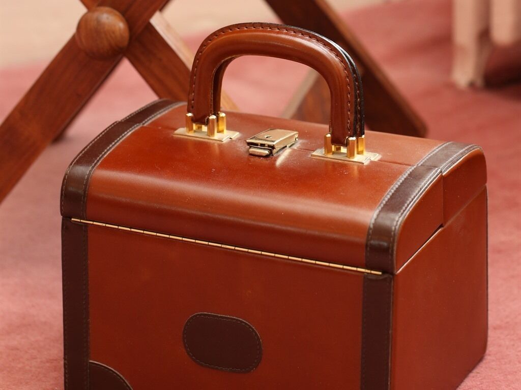 A brown suitcase with a handle and a lock, placed on a wooden chair.