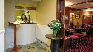 A reception area with a counter, a desk, a vase with flowers, and a dining area with chairs and tables. - The Argyll Hotel (Ullapool)