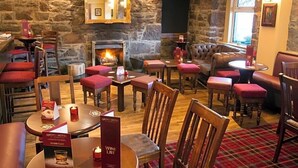 A cozy pub with stone walls, a fireplace, and red upholstered seating. - The Argyll Hotel (Ullapool)