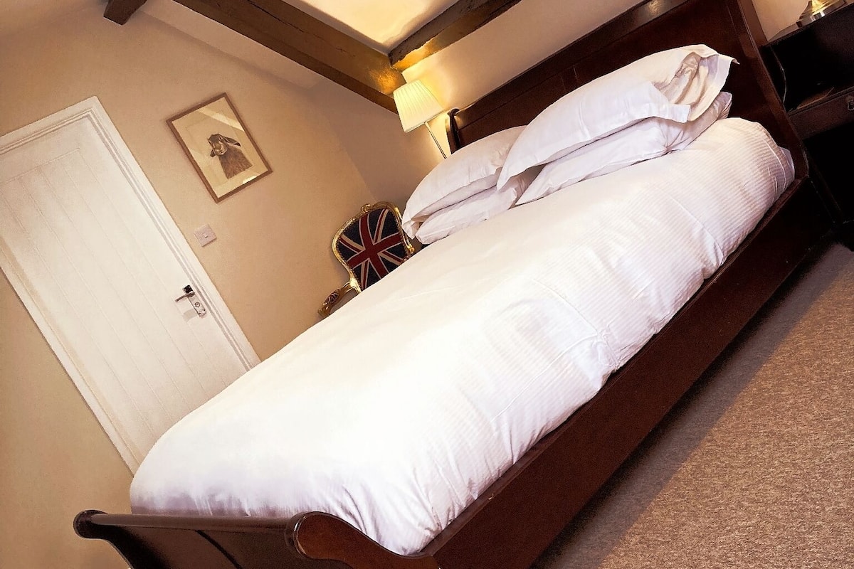 A bedroom with a wooden bed, white bedding, a bedside lamp, and a framed picture on the wall.
