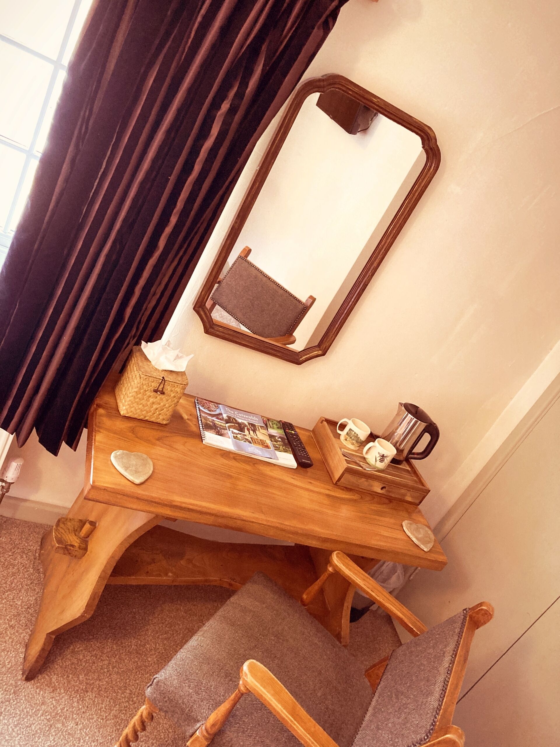 A wooden desk with a mirror, a book, a remote control, a coffee pot, and a tray with mugs.