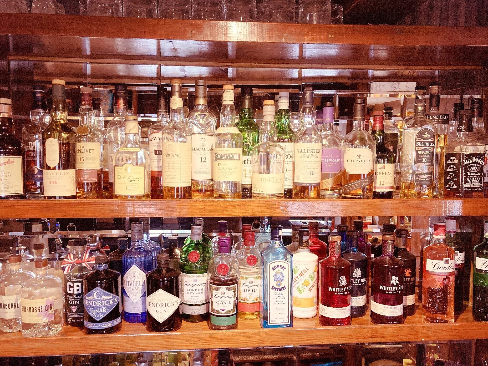 Un bar con estantes llenos de diversas botellas de alcohol, incluyendo ginebra, whisky y otras licores.