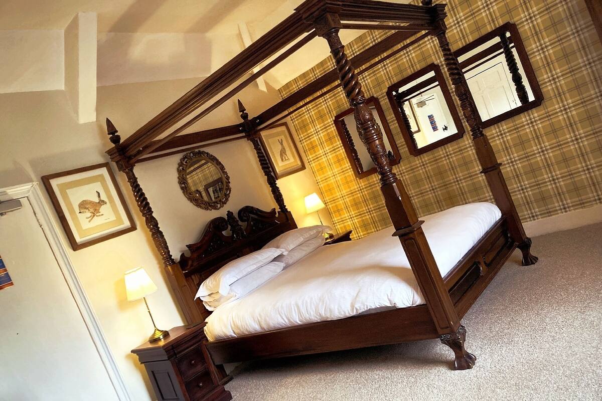 A four-poster bed with a wooden frame, a bedside table with a lamp, and a framed picture on the wall.