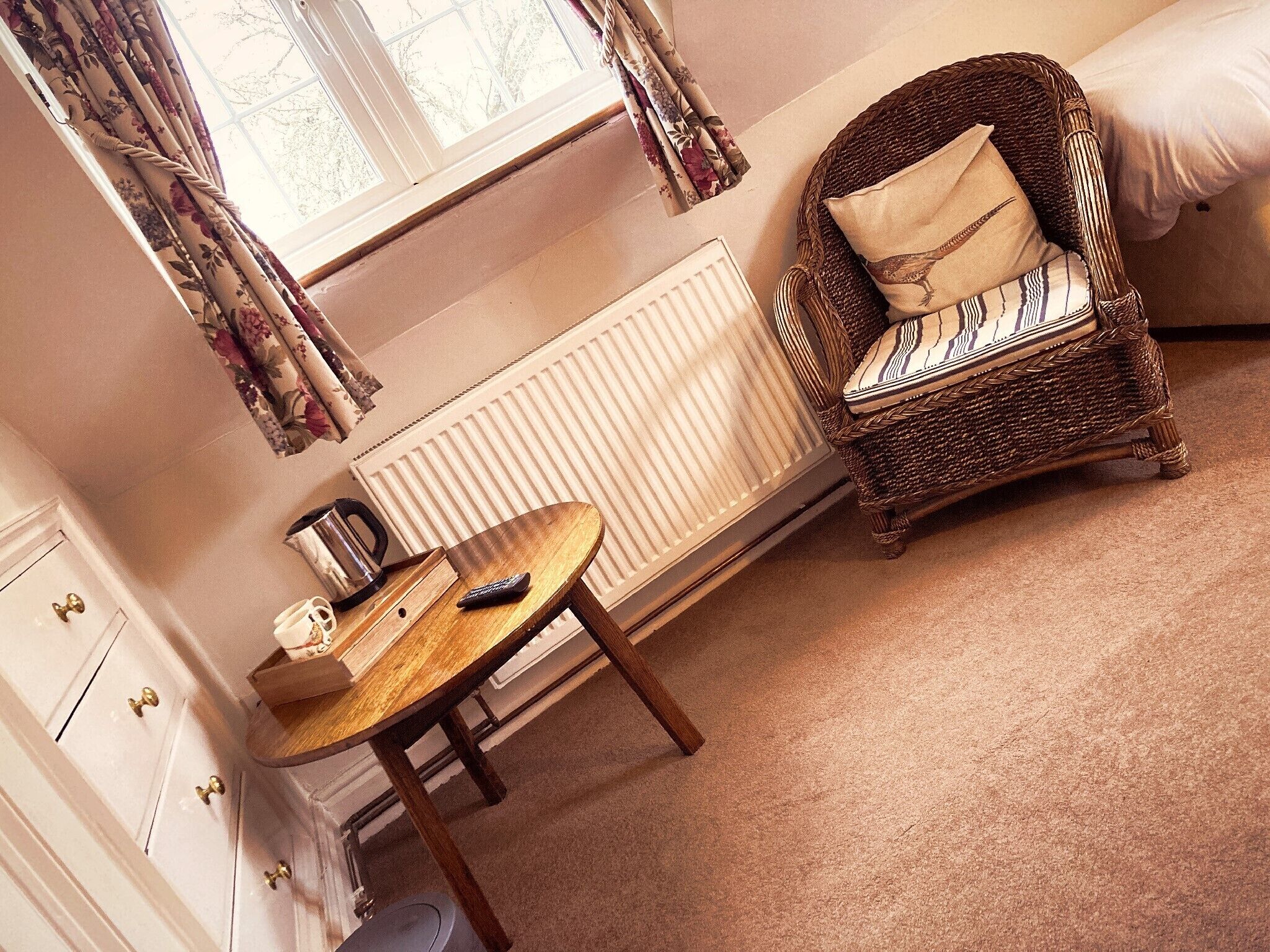A cozy room with a wicker chair, a small wooden table, and a radiator.