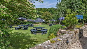 A garden area with picnic tables and umbrellas, a stone wall, and a sign indicating the entrance for residents. - Inn For All Seasons (Burford)