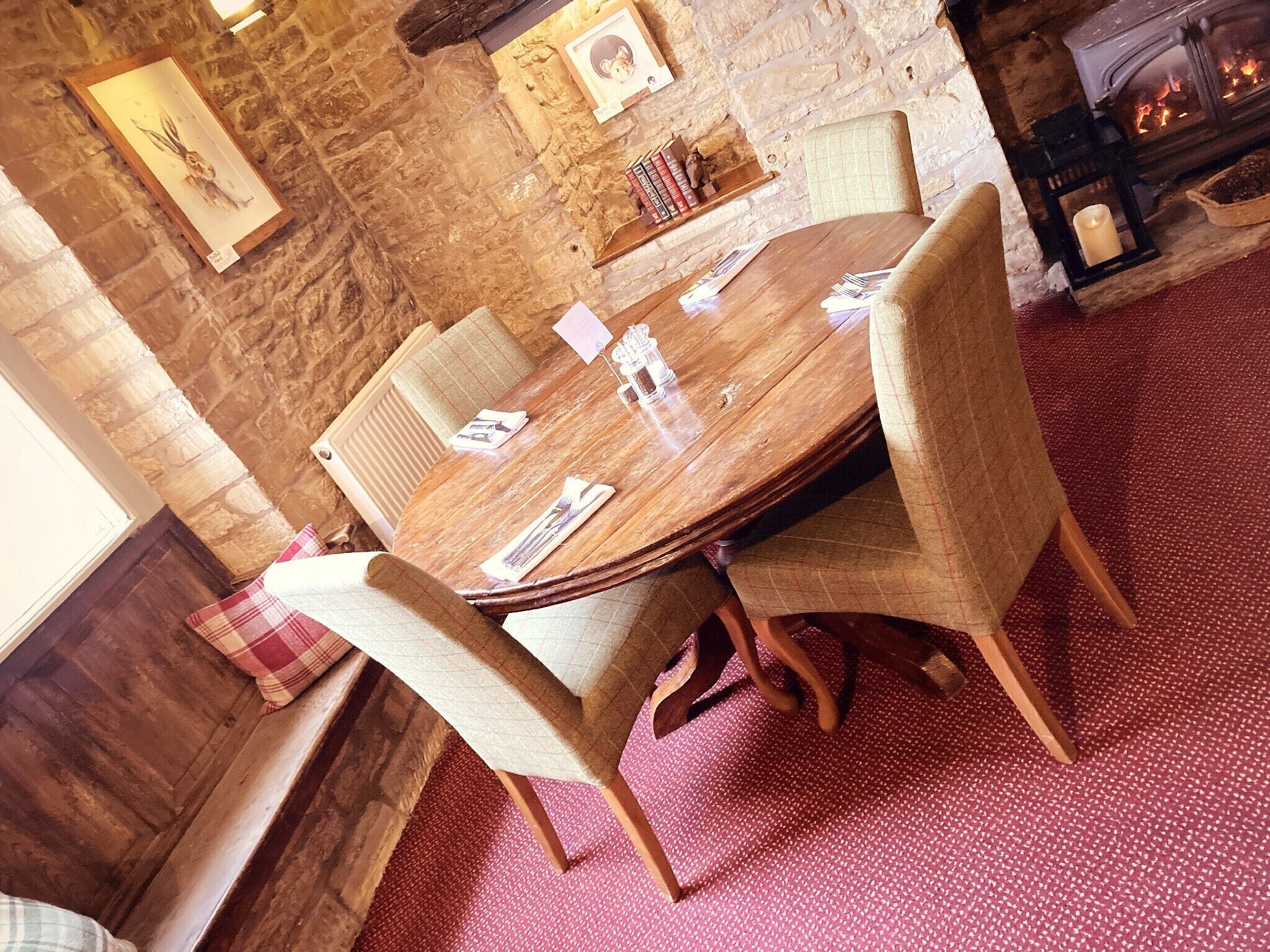 Una mesa de comedor de madera con sillas, una pared de piedra, una chimenea y un suelo cubierto de alfombra roja.