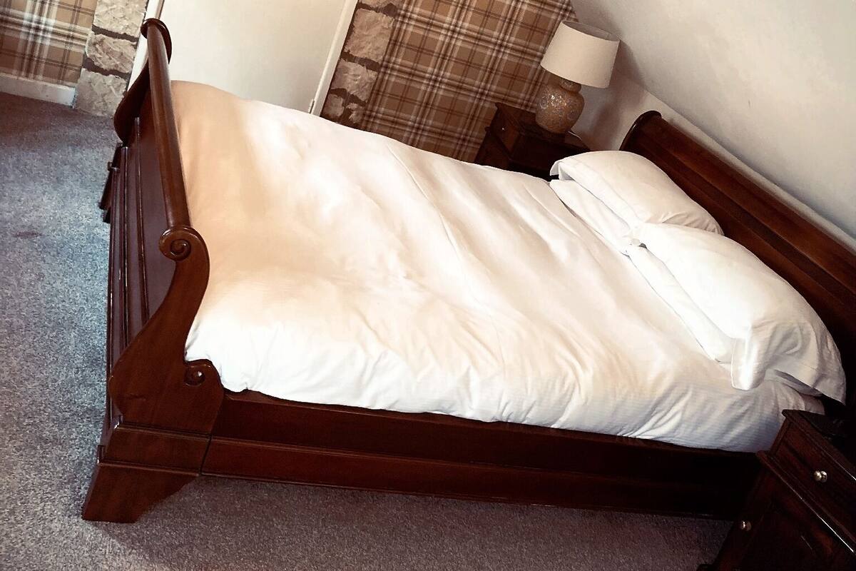 A bedroom with a wooden bed, a plaid curtain, and a stone wall.