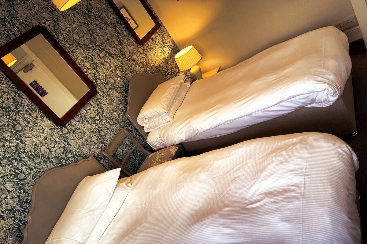 Two single beds with white linens, a mirror, and a lamp on a patterned carpet.