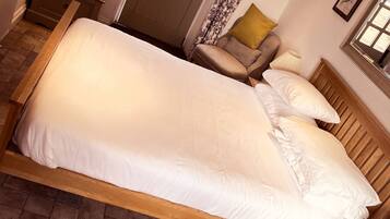 A neatly made bed with white linens, a wooden headboard, a bedside table with a lamp, and a door with a window.